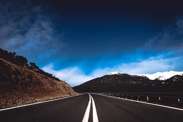 A mountain road with a view of a snowed mountain under the blue sky