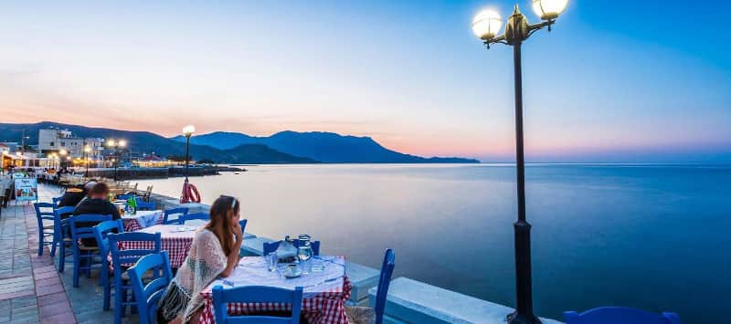 people siting at the tables of a sea side taverna in kissamos Chania on a summer evening