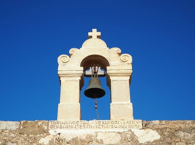 A stone belfry of a greek church under the blue sky, and a writing with details about the donor