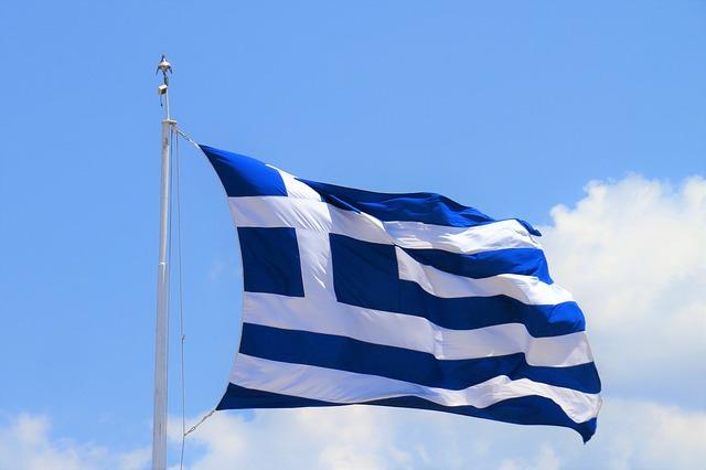 The Greek flag with blue and white stripes waving on the greek sky