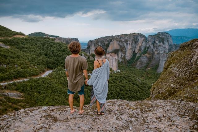 a couple standing on a cliff holding hands and admiring the mountainous views
