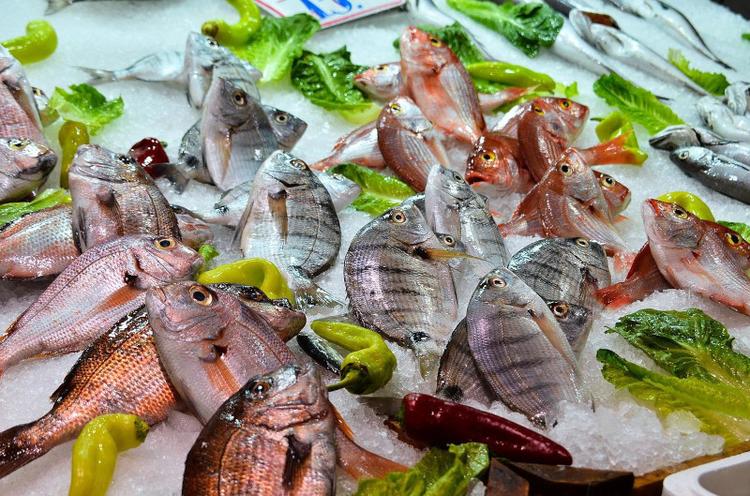 Various fish laying on ice among green peppers at a fish market stall