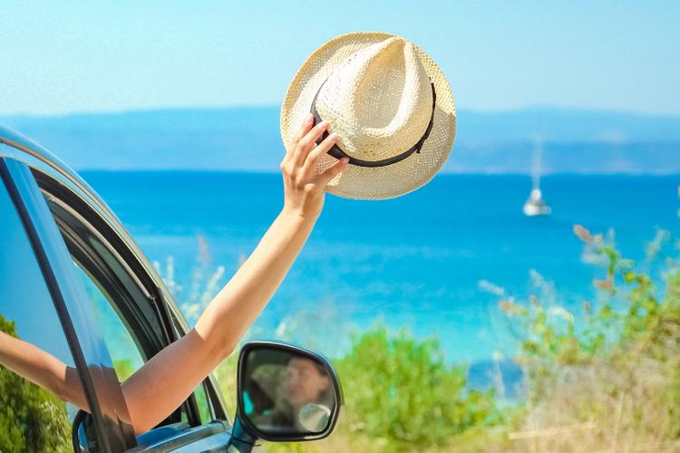 A woman raises her straw hat while she is looking at the sea inside her car