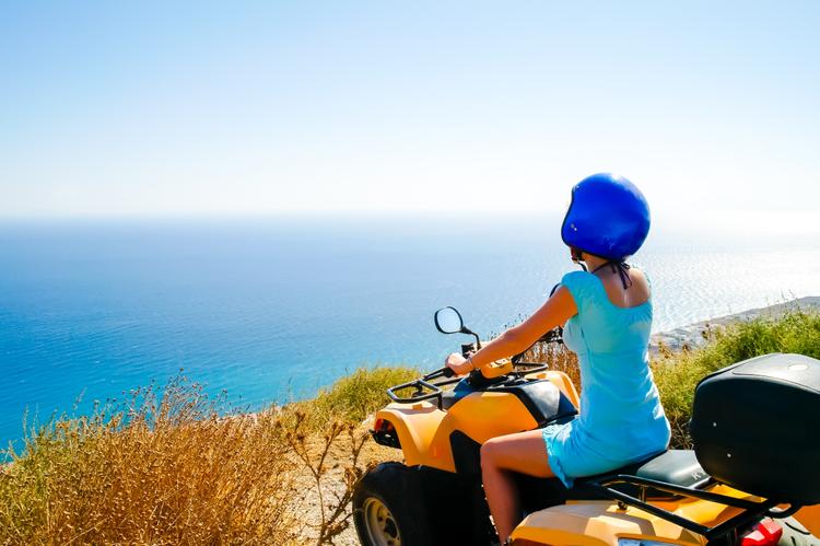 A woman in a blue dress riding an ATV overlooking the sea.